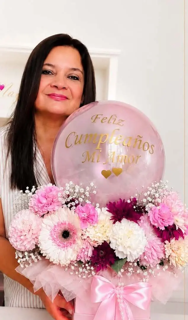 Mayina sosteniendo un bouquet de gerberas y claveles en tonos rosados con un globo que dice “Feliz Cumpleaños Mi Amor”.