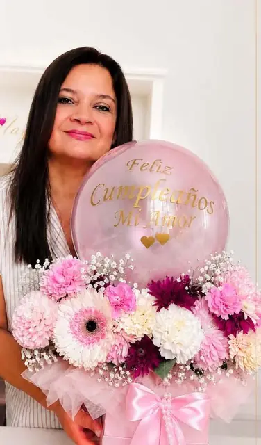 Mayina sosteniendo un bouquet de gerberas y claveles en tonos rosados con un globo que dice “Feliz Cumpleaños Mi Amor”.
