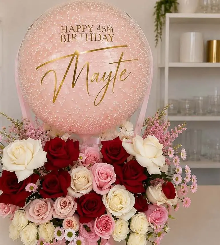 Arreglo de rosas rojas, blancas y rosadas con un globo transparente rosa que dice “Happy 45th Birthday Mayte” en letras doradas.