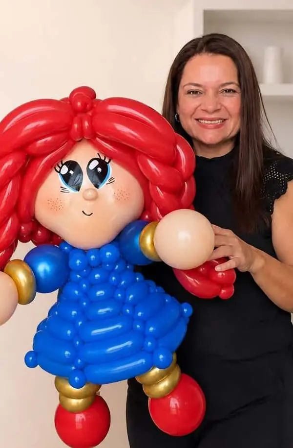 Sofía, una muñeca hecha con globos: cabello rojo trenzado, vestido azul y detalles dorados, sostenida por Mayina.