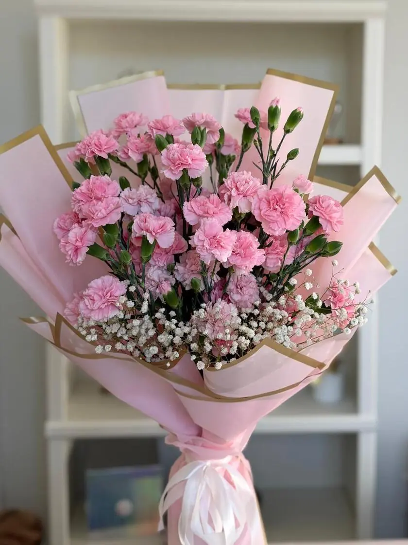 Ramo de claveles rosados con nube blanca, envuelto en papel rosa con filo dorado y atado con listón.